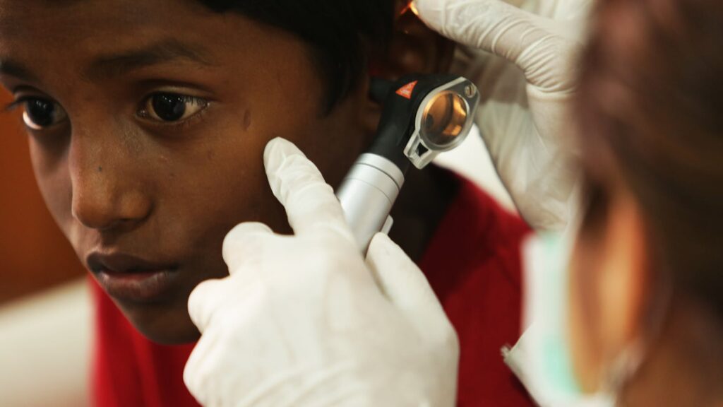 Un jeune garçon subit un examen de routine de l'oreille par un professionnel de la santé à l'aide d'un otoscope.