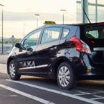 Photo réaliste d'un taxi électrique étiqueté comme service écologique, stationné devant l'entrée d'un terminal de l'aéroport Charles‑de‑Gaulle, avec une borne de recharge, un chauffeur professionnel et le skyline de Paris en arrière‑plan.
