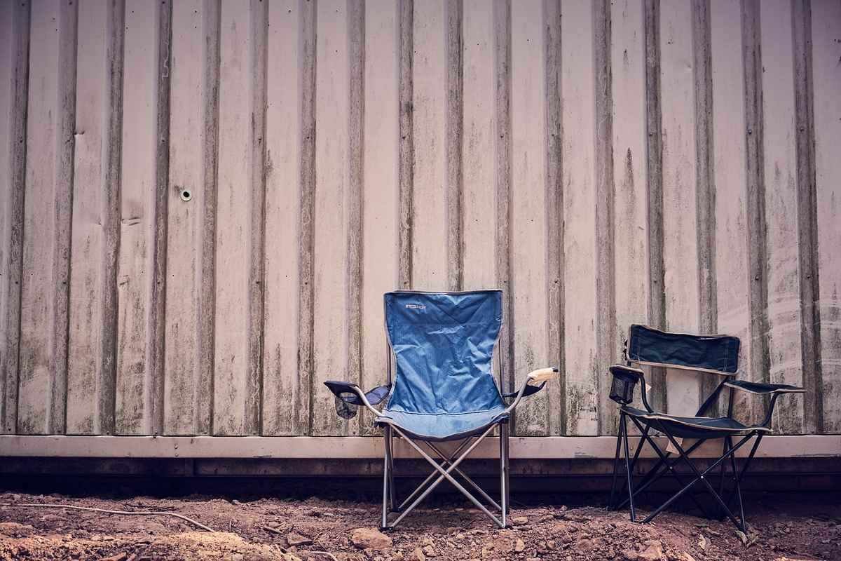Deux fauteuils pliants bleus et noirs devant une muraille en tôle ondulée