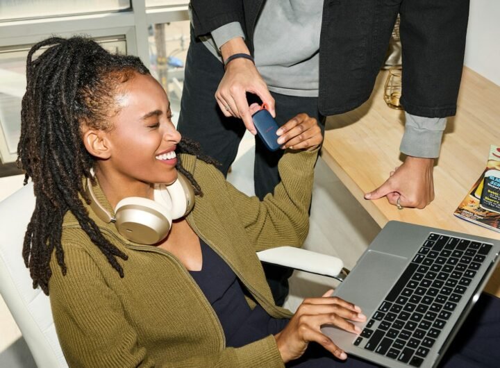 Smiling woman uses laptop, person holds credit card nearby