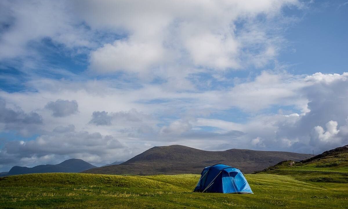 Un tente bleue solitaire sur prairie verdoyante, montagnes lointaines, ciel nuageux