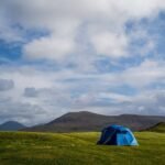 Un tente bleue solitaire sur prairie verdoyante, montagnes lointaines, ciel nuageux