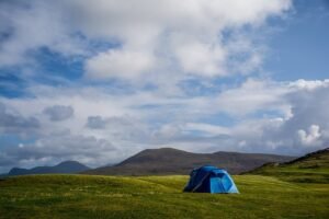 Un tente bleue solitaire sur prairie verdoyante, montagnes lointaines, ciel nuageux