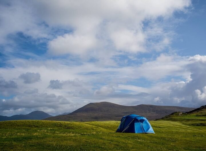 Un tente bleue solitaire sur prairie verdoyante, montagnes lointaines, ciel nuageux