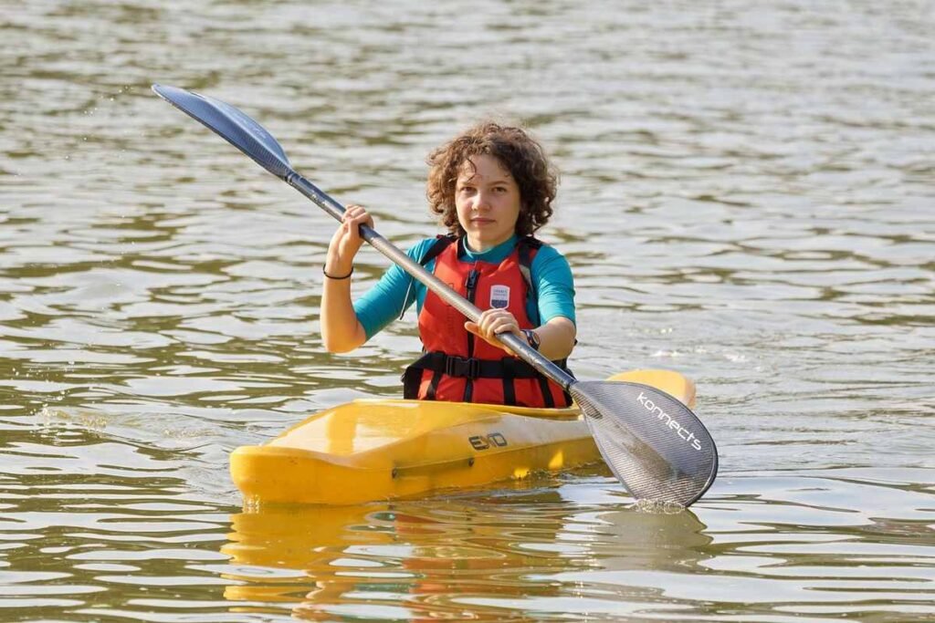 Enfant rieur dans kayak jaune, pagaie à l'eau, gilet orange