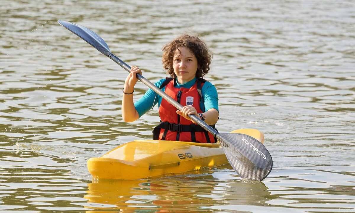 Enfant rieur dans kayak jaune, pagaie à l'eau, gilet orange