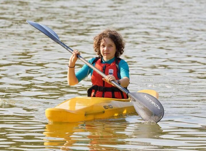 Enfant rieur dans kayak jaune, pagaie à l'eau, gilet orange