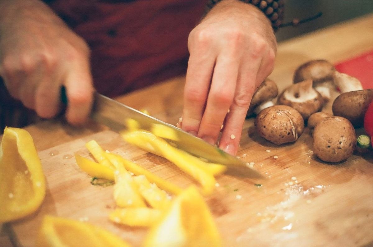 Personne tranchant des poivrons jaunes et des champignons sur une planche en bois Personne tranchant des poivrons jaunes et des champignons sur une planche en bois