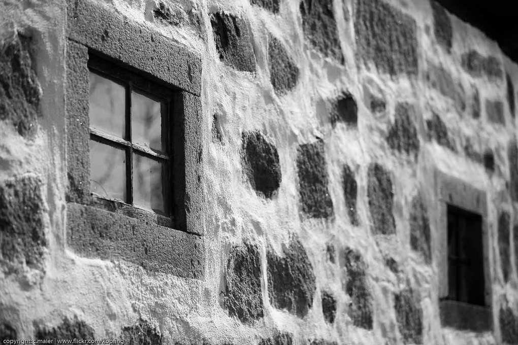 Mur de pierre blanche avec deux fenêtres carrées et texture granuleuse apparente