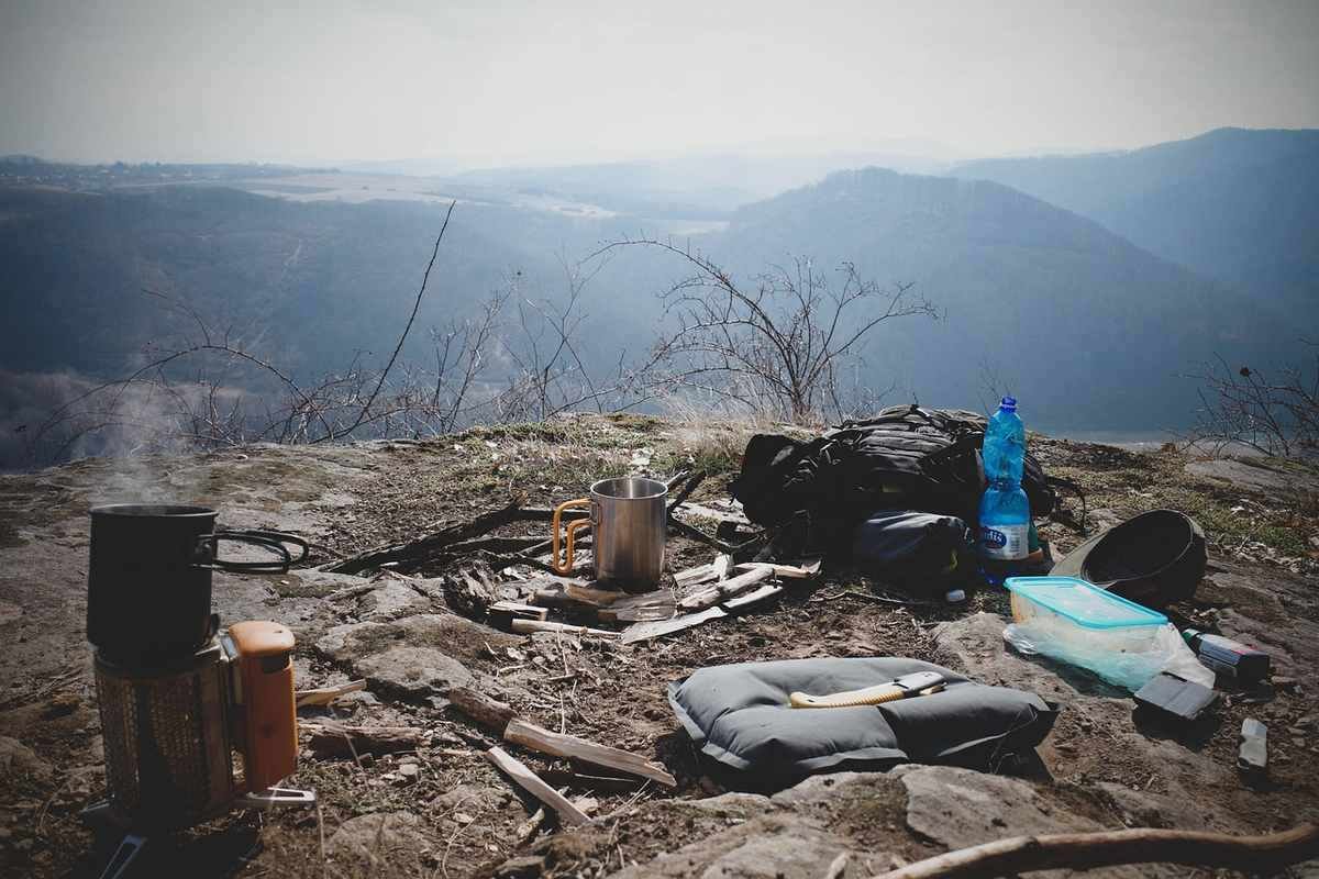 Campement en montagne avec équipement de survie, sacs, gourde et ustensiles de cuisine dispersés sur le sol