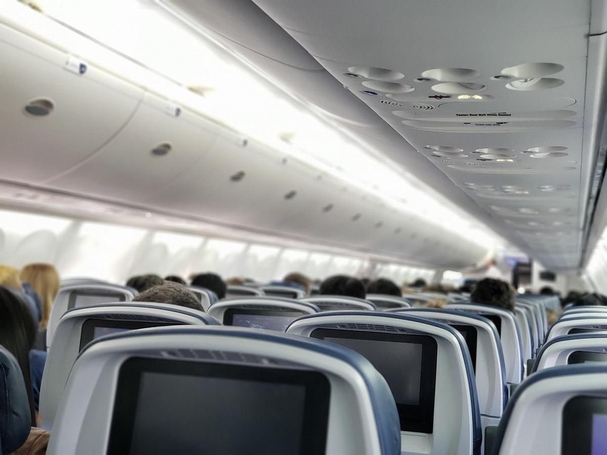 Intérieur d'avion avec sièges et écrans, passagers assis, vue du couloir